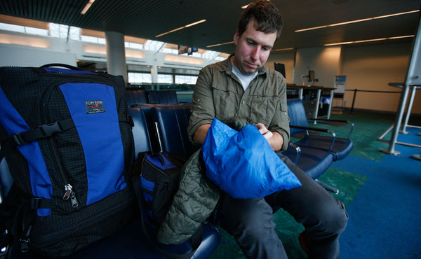 A person stuffing the Pocket Travel Pillow with a padded jacket.